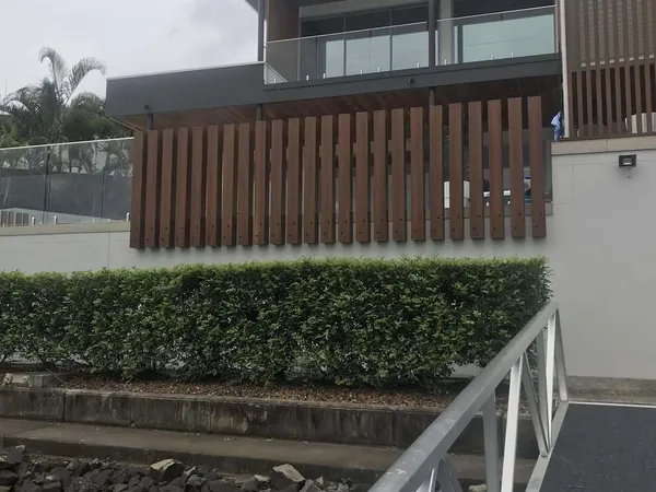 Woodgrain aluminium batten screen above a hedge on a white boundary wall