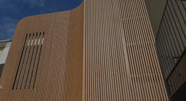 Tall facade fully clad in pale woodgrain aluminium vertical battens